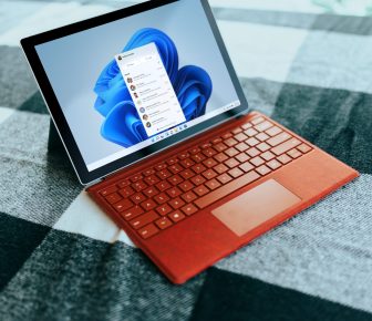 Red Surface laptop on a checkered bed by a window